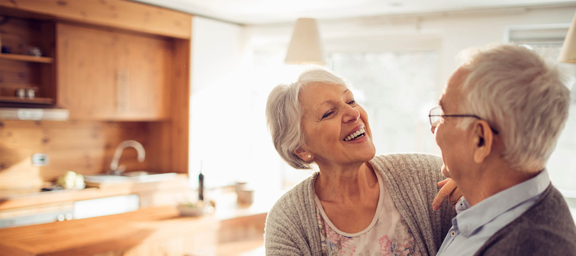 Mature couple dancing in sunny kitchen.