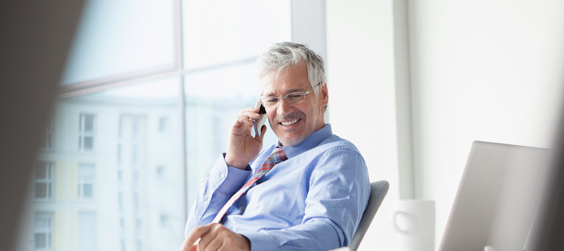 Man smiling while talking on the phone in a well lit sunny office.